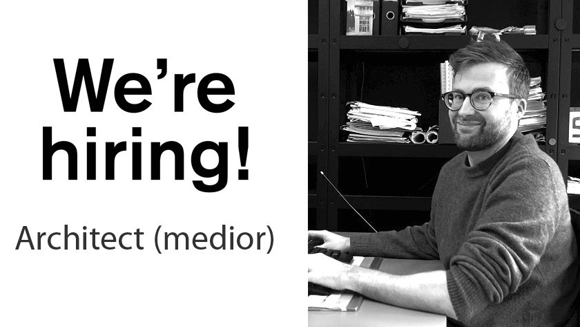 We're hiring! Architect (medior) — man at a desk in an office, smiling at the camera.