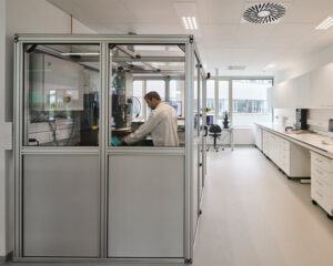 Scientist in a white lab coat works inside a glass-enclosed cabinet in a modern laboratory.