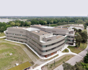Aerial view of a curved beige office building on a green campus with walkways and trees nearby.