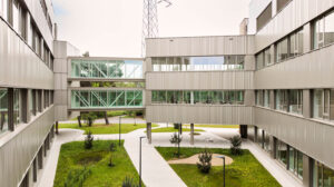 Modern office building with metal cladding and a glass skybridge over a grassy courtyard.