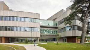 Modern multi-story office building with glass skybridge, a person walking on a curved concrete path