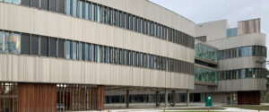 Modern office building with light gray metal panels and long rows of windows.