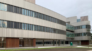 Modern multi-story building with silver metal cladding, long rows of windows and a curved glass corner.